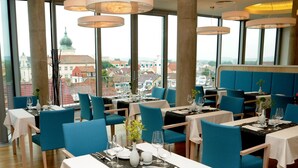 A restaurant with tables set for dining, large windows offering a city view, and modern pendant lighting. - Hotel Erwin Junker (Holice)