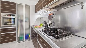Moderni keittiö, jossa on sisäänrakennettu uuni, ruostumattomasta teräksestä valmistetut työtasot ja kaasuliesi.