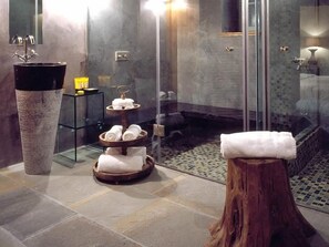 A modern bathroom with a stone sink, a glass shower enclosure, and a wooden stool with a towel. - 5 Senses (Zagori)