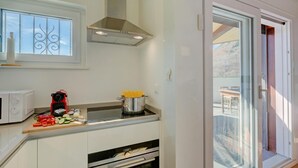 Eine Küche mit Mikrowelle, einem roten Gerät, einem Topf mit Pasta und einem Schneidebrett mit Gemüse.