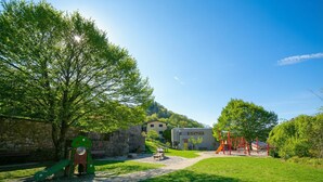 Ein Park mit Spielgeräten, einer Steinmauer und einem Gebäude im Hintergrund.