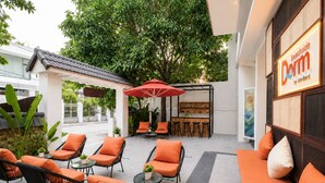 Un espacio al aire libre con sillas de mimbre y cojines naranjas, una sombrilla roja y una zona de bar con taburetes.