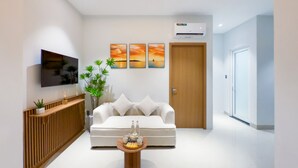 Una sala moderna con un sofá, una mesa de centro con una bandeja de objetos, un televisor montado en la pared y una puerta con un equipo de aire acondicionado.