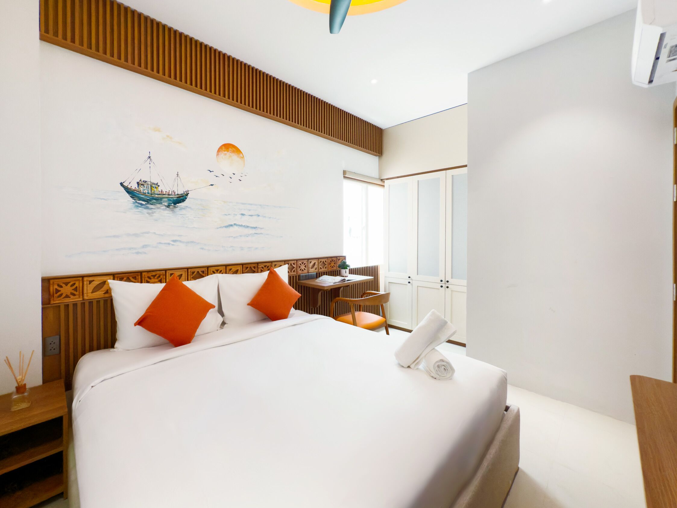A hotel room with a bed, a desk, a chair, a window, and a painting on the wall.