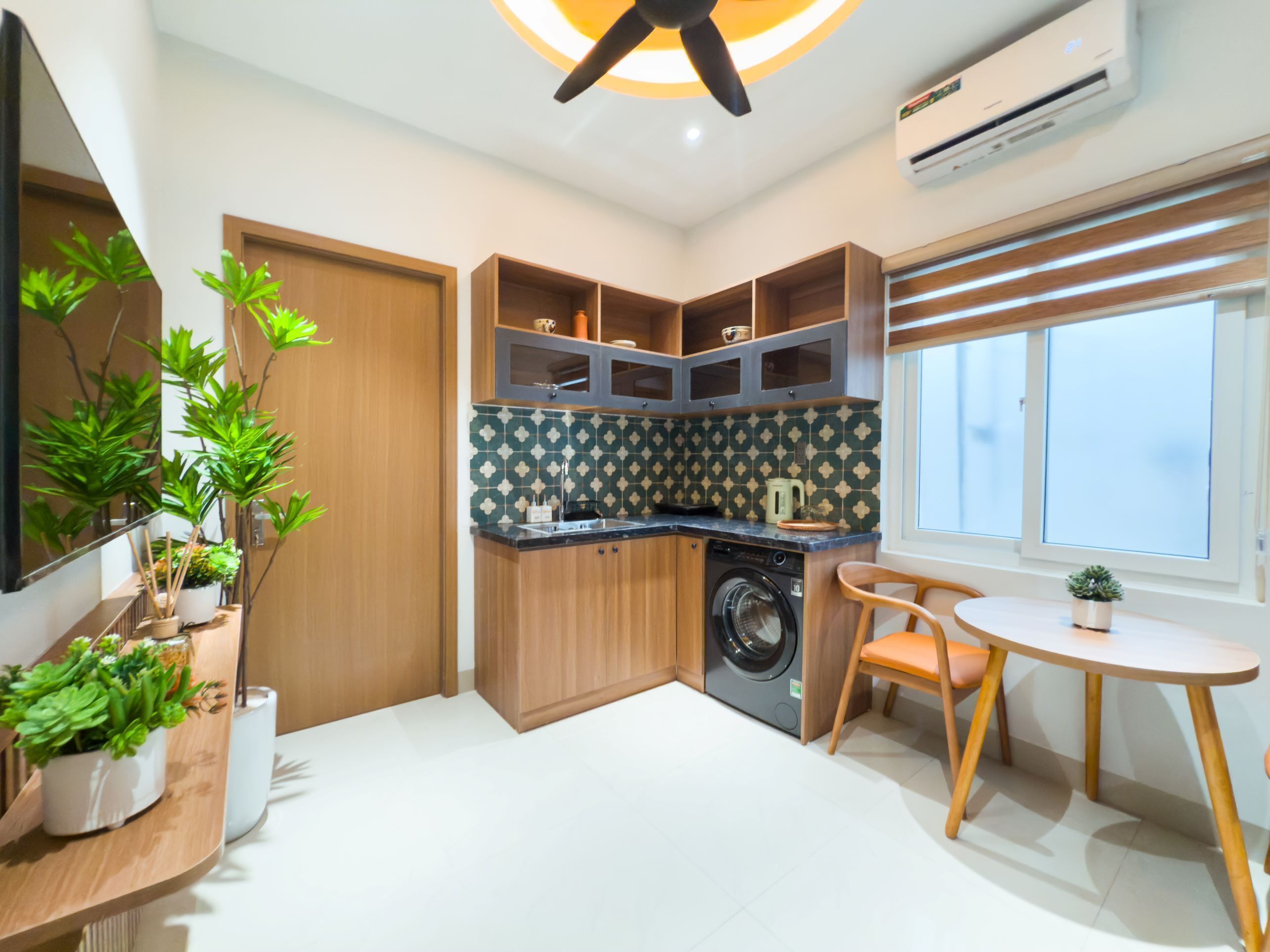 A compact kitchen with a washing machine, wooden cabinets, and a dining area with a small table and chair.