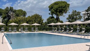 A swimming pool with lounge chairs and umbrellas, surrounded by trees and a clear sky. - Eraora Hotel Village (Battipaglia)