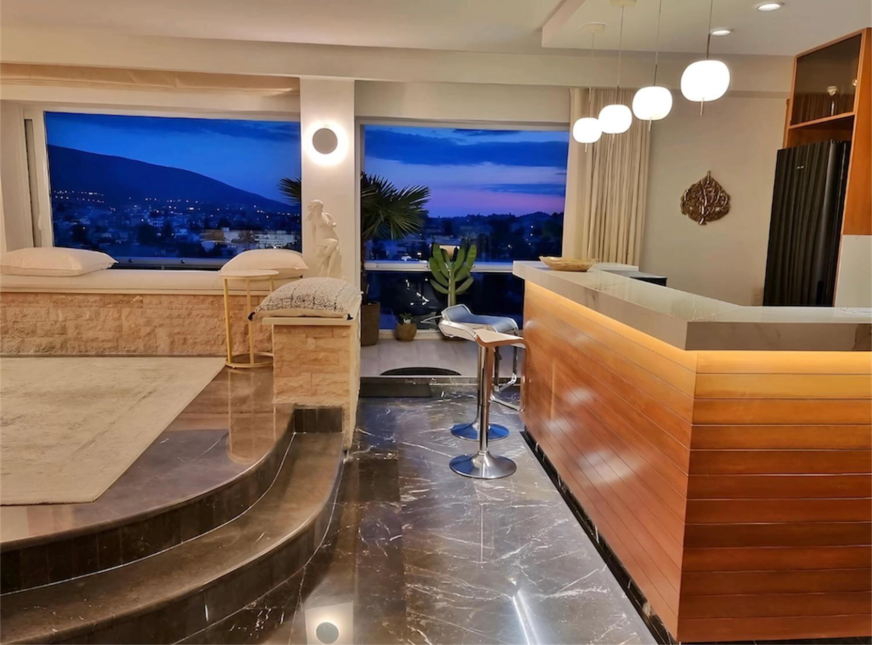 Una moderna camera d'albergo con balcone, una reception e un'area salotto con vista sulla città.