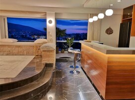 Habitación de hotel moderna con balcón, un mostrador de recepción y una zona de estar con vistas a la ciudad.