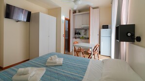 Habitación de hotel con cama, televisor de pantalla plana, ventilador de techo, kitchenette y baño.