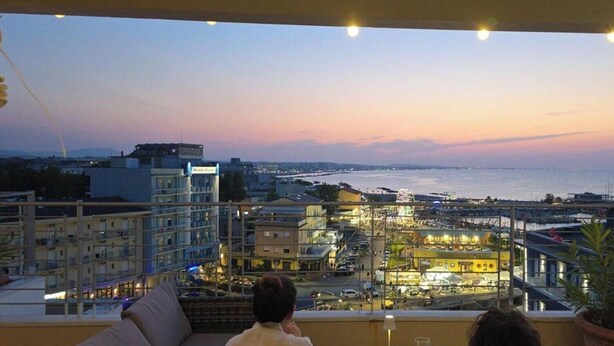 Un balcón con vistas a un paisaje urbano al atardecer, que incluye edificios y una masa de agua.