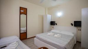 Una habitación de hotel con cama, una silla, escritorio, espejo, ventilador de techo y televisor.