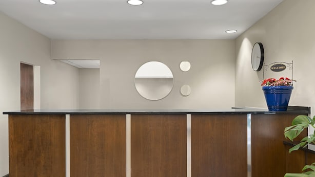 A reception desk with a wooden finish, three ceiling lights, and a welcome sign. - Larkspur Landing Hotel South Bend (South Bend)