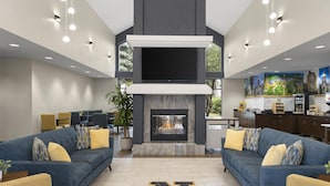 A modern living room with a fireplace, two sofas, a coffee table, and a dining area. - Larkspur Landing Hotel South Bend (South Bend)