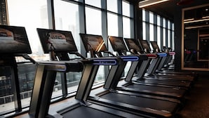 A row of treadmills with digital displays, positioned in a room with large windows offering a city view. - The E11EVEN Hotel & Residences (Miami)