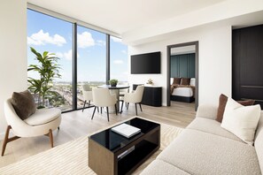 A modern living room with a large window, a flat-screen TV, a sofa, a coffee table, and a dining area with chairs.