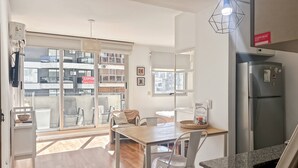 Eine moderne Küche mit integriertem Kühlschrank, ein Essbereich mit Holztisch und weißen Stühlen sowie große Fenster mit Blick auf die Stadt.