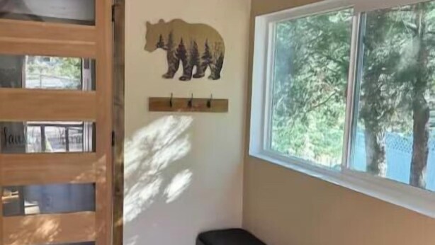 Una habitación con un banco de madera, un adorno de oso en la pared, una ventana con vistas a árboles y una puerta con paneles de vidrio.
