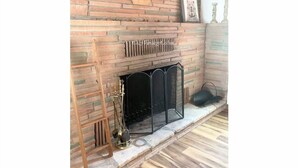 Una chimenea con pared de piedra, una escalera de madera y una reja metálica.