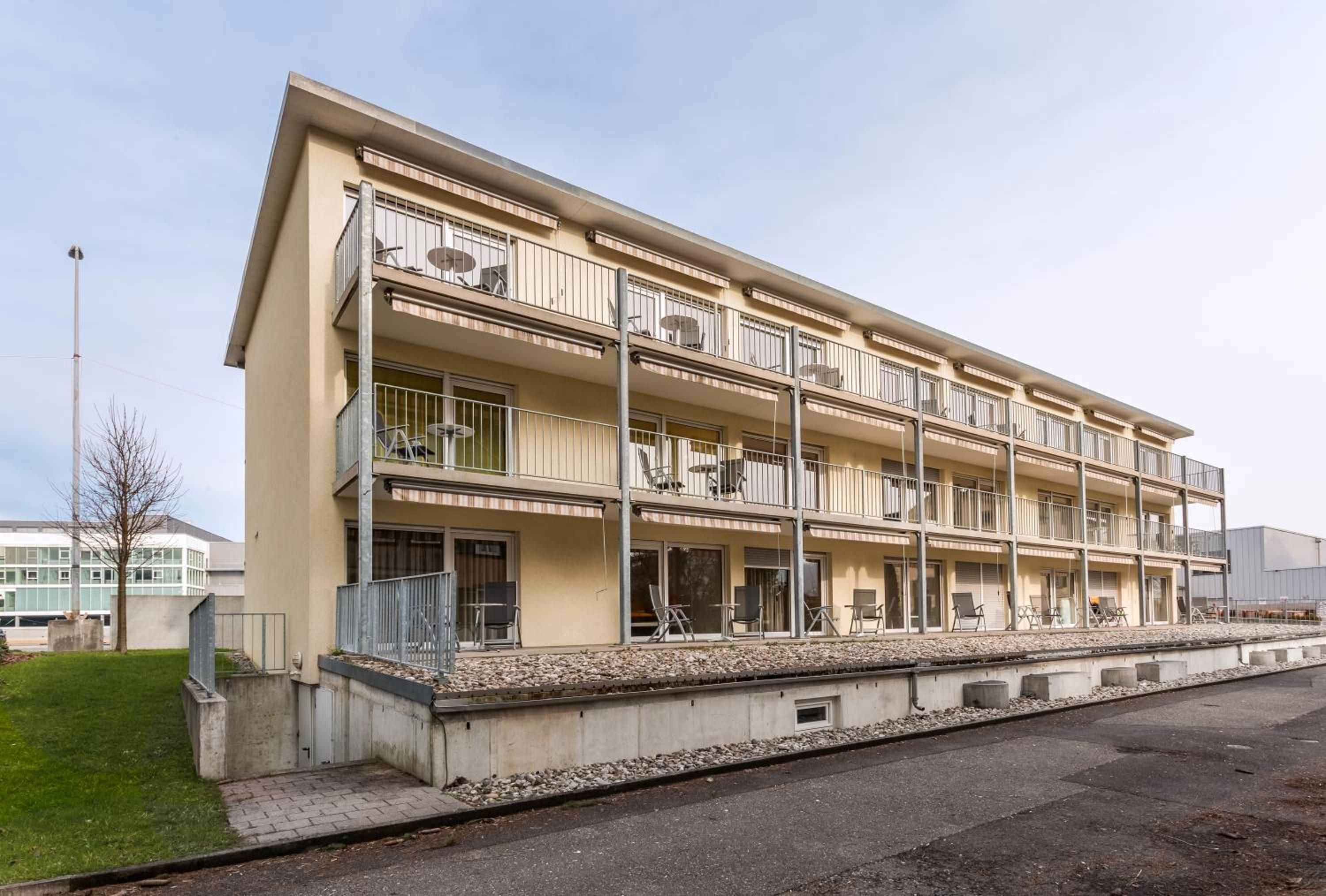 Un edificio de varios pisos con balcones, mobiliario exterior y techo plano.