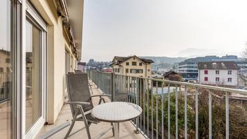 Ein Balkon mit Tisch und Stühlen, der auf einen Stadtblick mit Gebäuden und einem Fluss blickt.