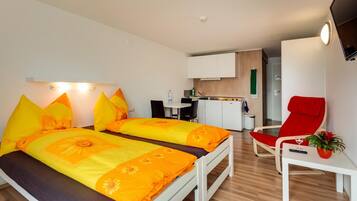 Ein modernes Hotelzimmer mit einem Bett, einem Schreibtisch, einem Sessel, einer Küchenzeile und einem Fernseher.