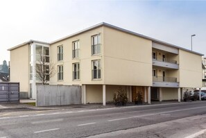 En flervåningsbyggnad med bostäder, kännetecknad av en slät fasad, stora fönster och en balkong på översta våningen.