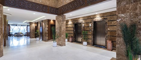 A spacious lobby with a high ceiling, marble walls, and a central elevator area.