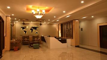 A lobby with a reception desk, seating area, world map wall, ceiling fans, and a staircase.