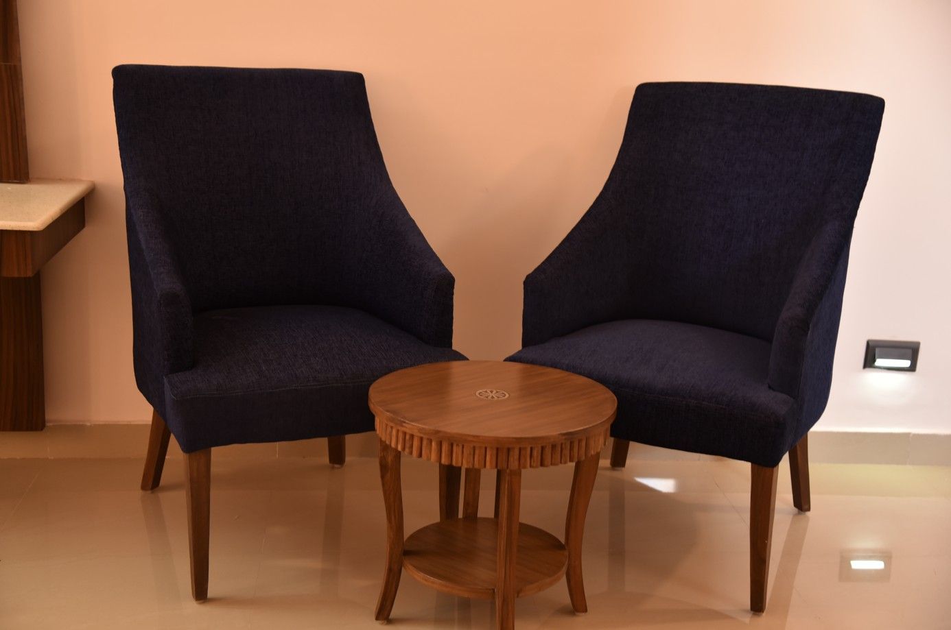 Dos sillones azul oscuro con patas de madera y una mesita redonda de madera en el centro.