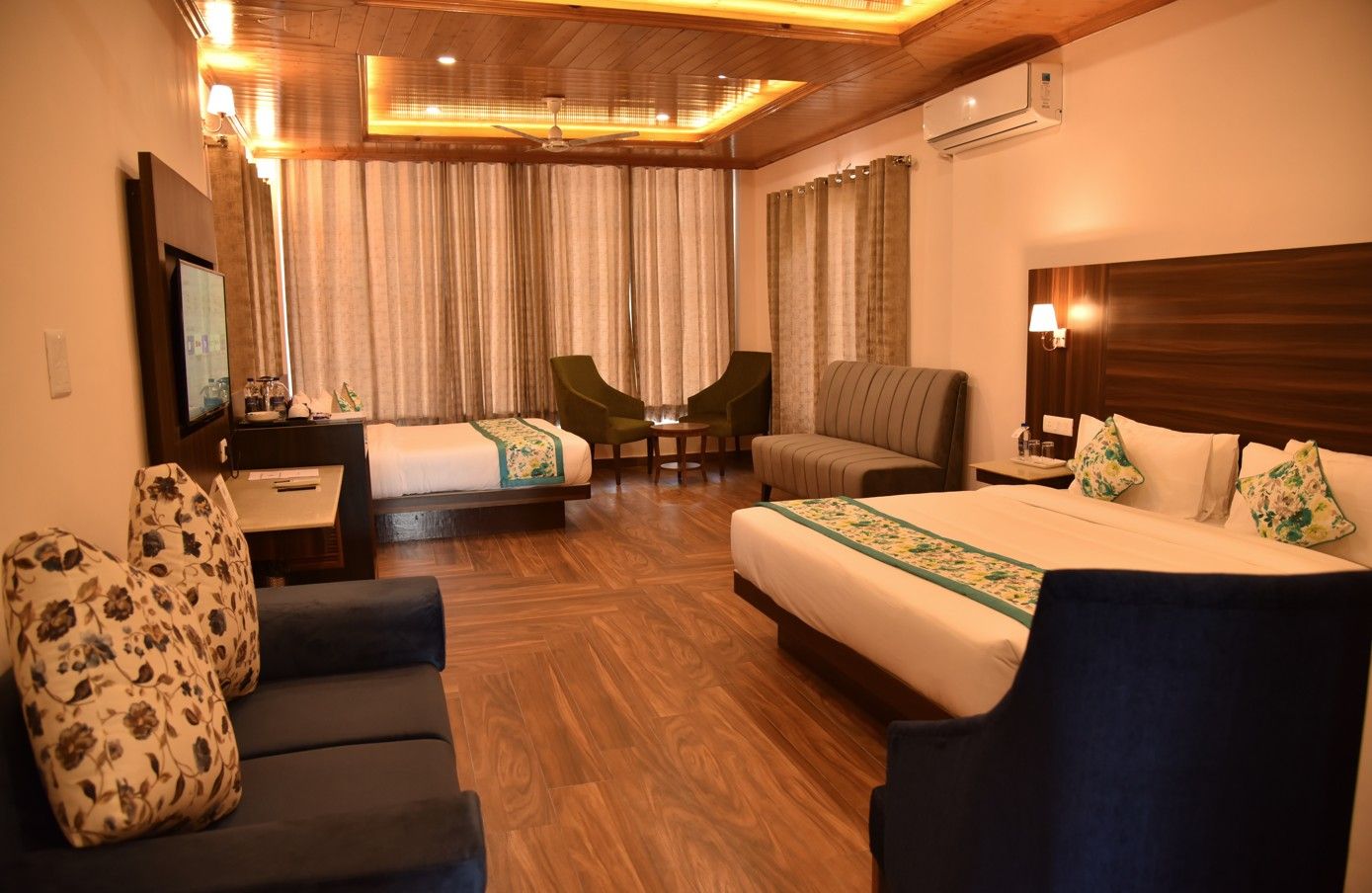 A hotel room with a bed, two armchairs, a sofa, a desk with a flat-screen TV, and a ceiling fan.