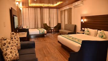 A hotel room with a bed, two armchairs, a sofa, a desk with a flat-screen TV, and a ceiling fan.