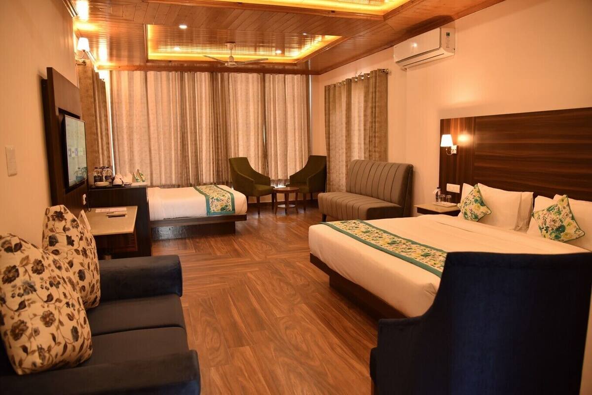 A hotel room with a bed, two armchairs, a sofa, a desk with a flat-screen TV, and a ceiling fan.