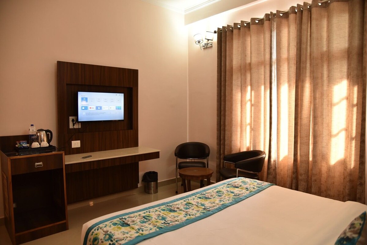 A hotel room with a bed, a desk, a chair, a television, and curtains.
