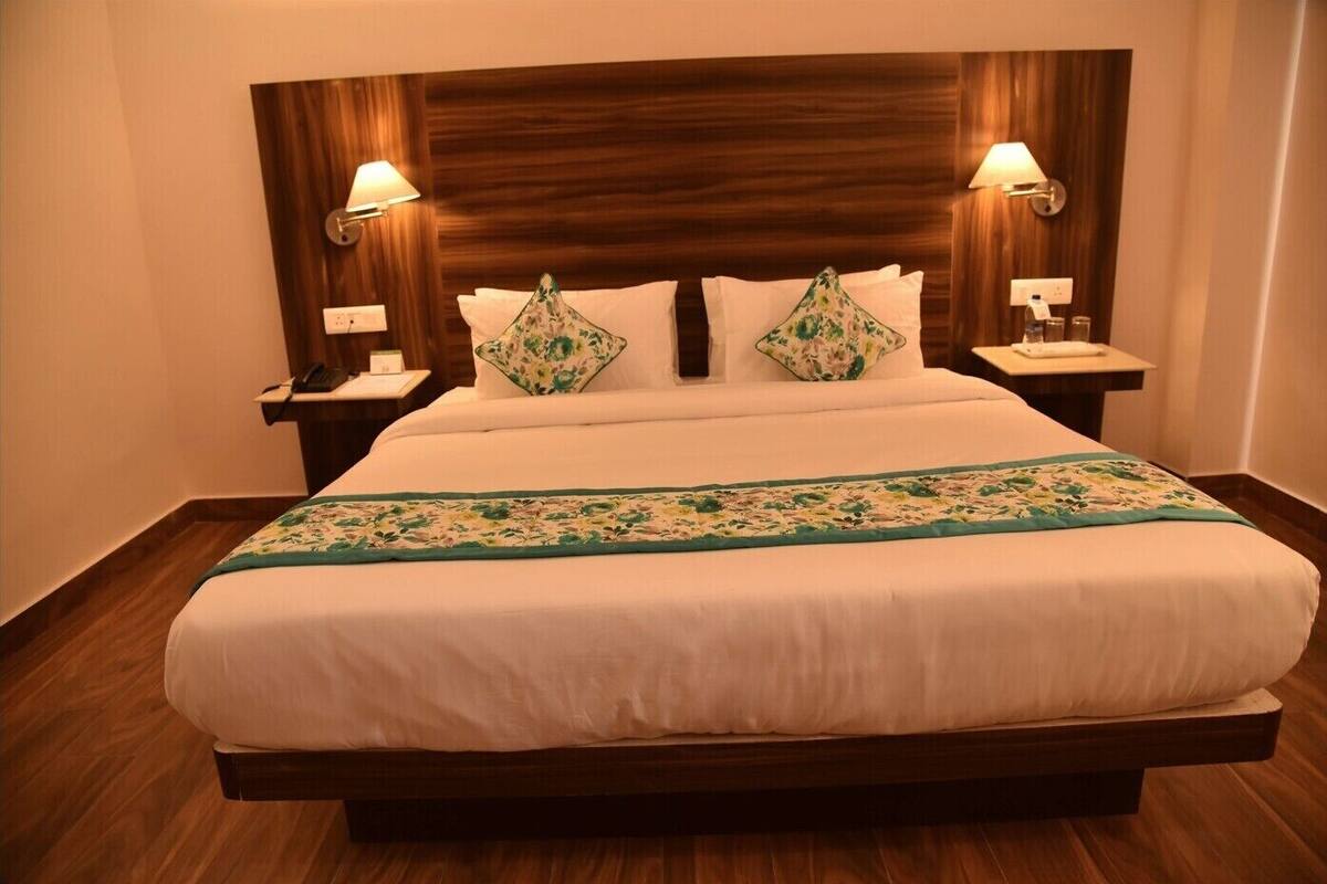 A hotel room with a large bed, wooden headboard, two bedside lamps, and a floral bedspread.