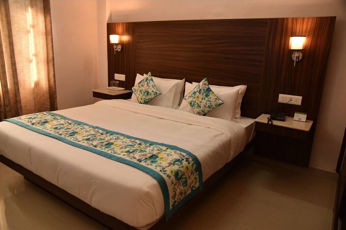A hotel room with a large bed, two bedside tables with lamps, a wooden headboard, and a floral bedspread.