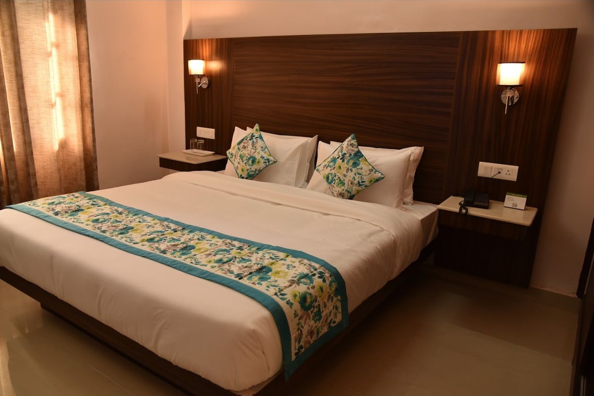 Een hotelkamer met een groot bed, twee nachtkastjes met lampen, een houten hoofdeinde en een bloemenprint bedspreider.