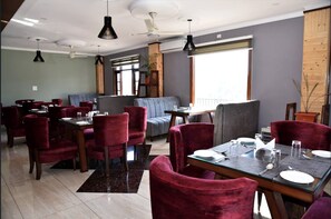 A restaurant with red chairs, tables set for dining, and a large window providing natural light. - Mastiff Wildcrest Dharamshala by Othpl (Palampur)