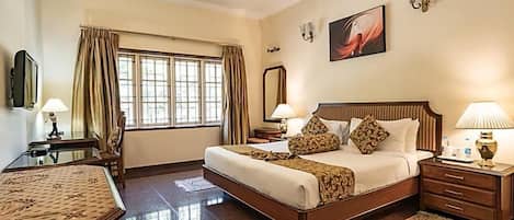 A hotel room with a bed, bedside tables, a desk, a chair, a window with curtains, a ceiling fan, and a painting on the wall.