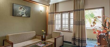 A hotel lobby with a sofa, armchair, coffee table, and a painting on the wall.