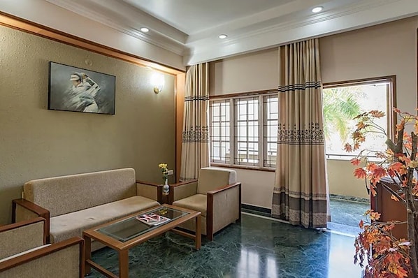 A hotel lobby with a sofa, armchair, coffee table, and a painting on the wall. - Eagleton The Golf Resort (Ramanagara)