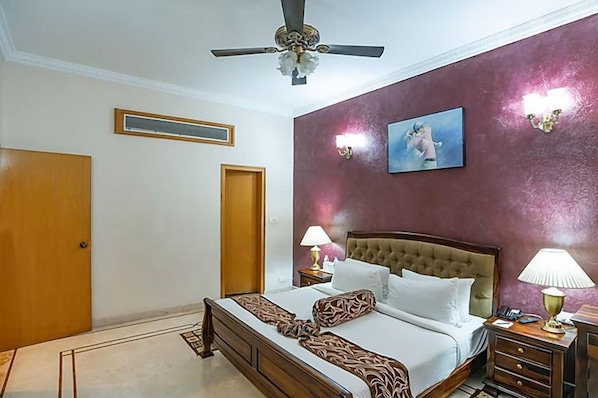 A hotel room with a bed, a ceiling fan, a painting on the wall, and two bedside lamps. - Eagleton The Golf Resort (Ramanagara)
