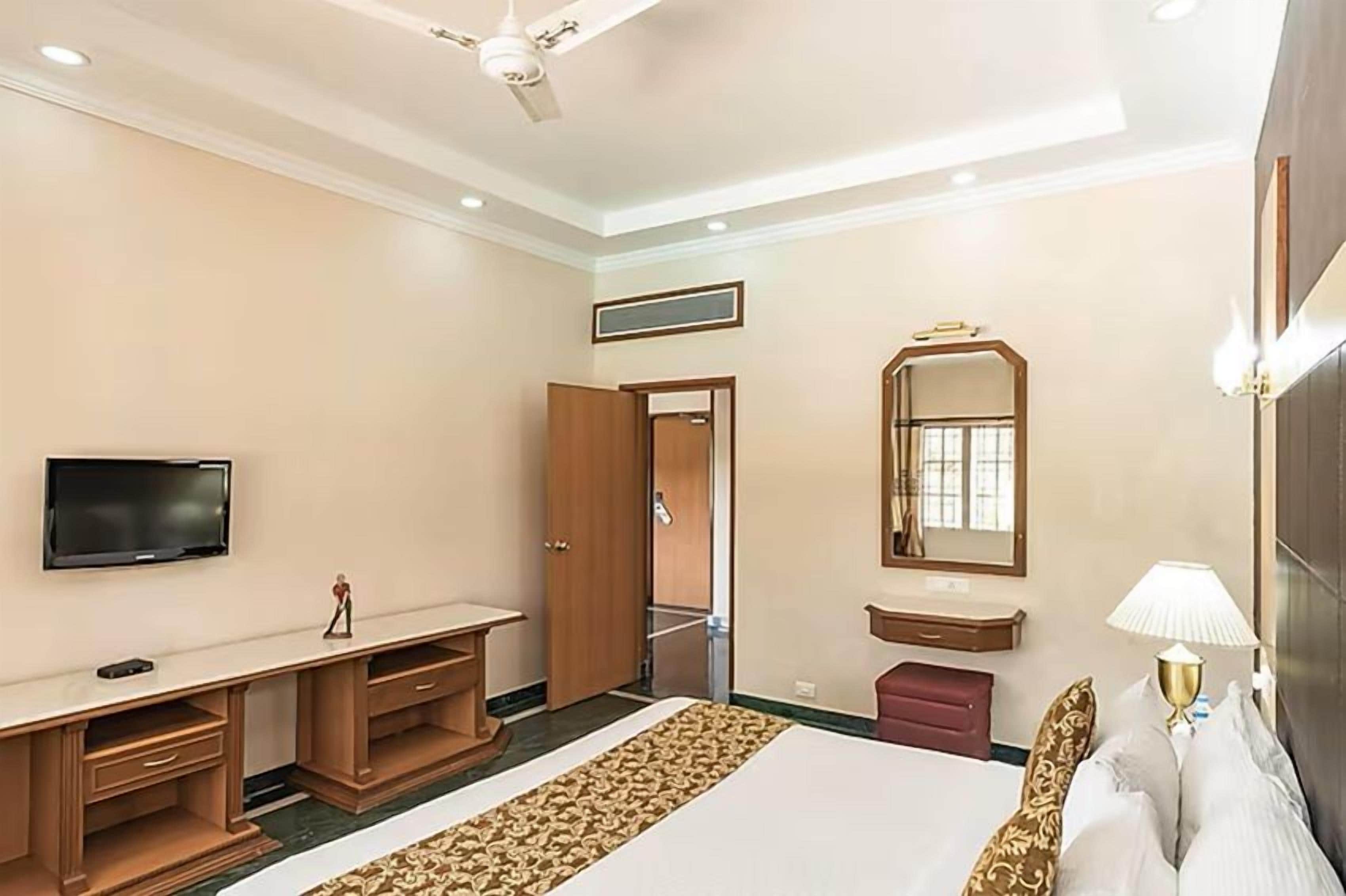 A hotel room with a bed, a desk, a television, a mirror, and a ceiling fan.