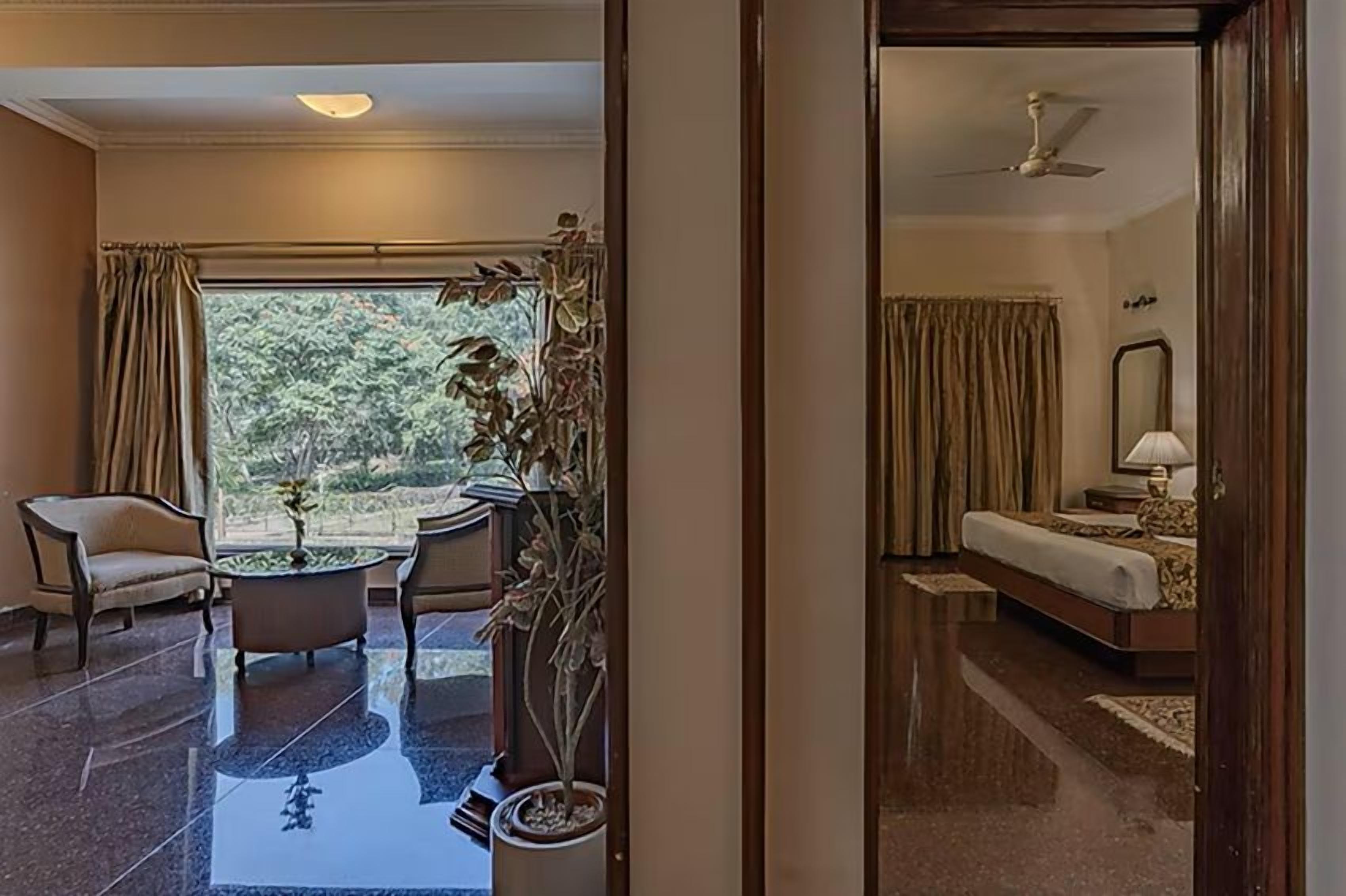Ein Hotelzimmer mit Bett, Schreibtisch, Stuhl, Blumentopf und Blick ins Freie.