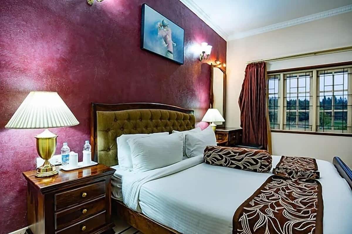 Hotellihuone, jossa on suuri sänky, kaksi yöpöytää, sängynpääty, ikkuna, jossa on verhot, ja seinälle kiinnitetty taulu.