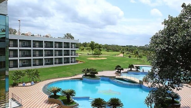 A hotel with a large pool, a golf course, and a building with multiple balconies. - Eagleton The Golf Resort (Ramanagara)