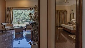 A hotel room with a bed, a desk, a chair, a potted plant, and a view of the outdoors. - Eagleton The Golf Resort (Ramanagara)