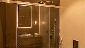 A modern bathroom with a glass-enclosed shower, a sink, and a toilet. - Eagleton The Golf Resort (Ramanagara)