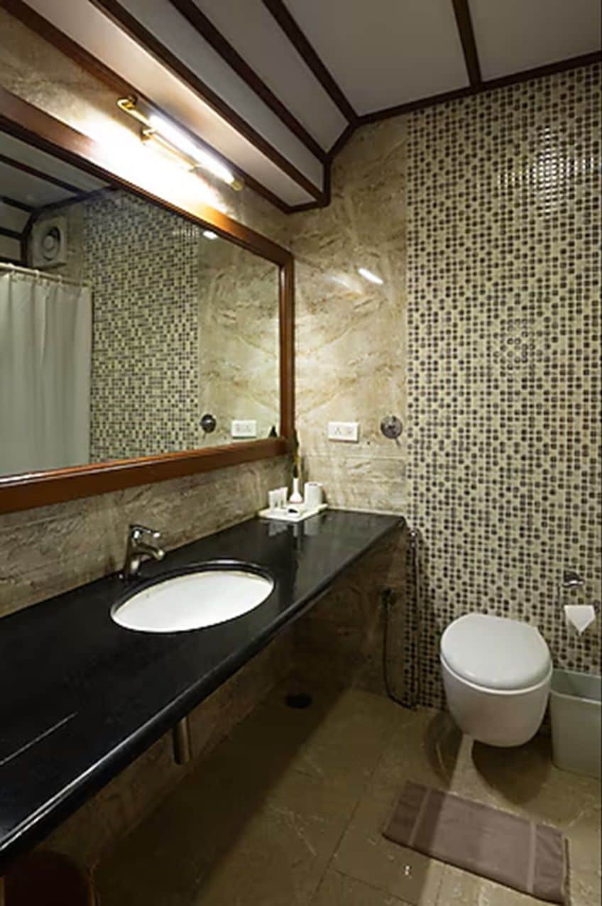 Ein Badezimmer mit Waschbecken in Schwarz, einem Spiegel, einer Toilette und gefliesten Wänden.