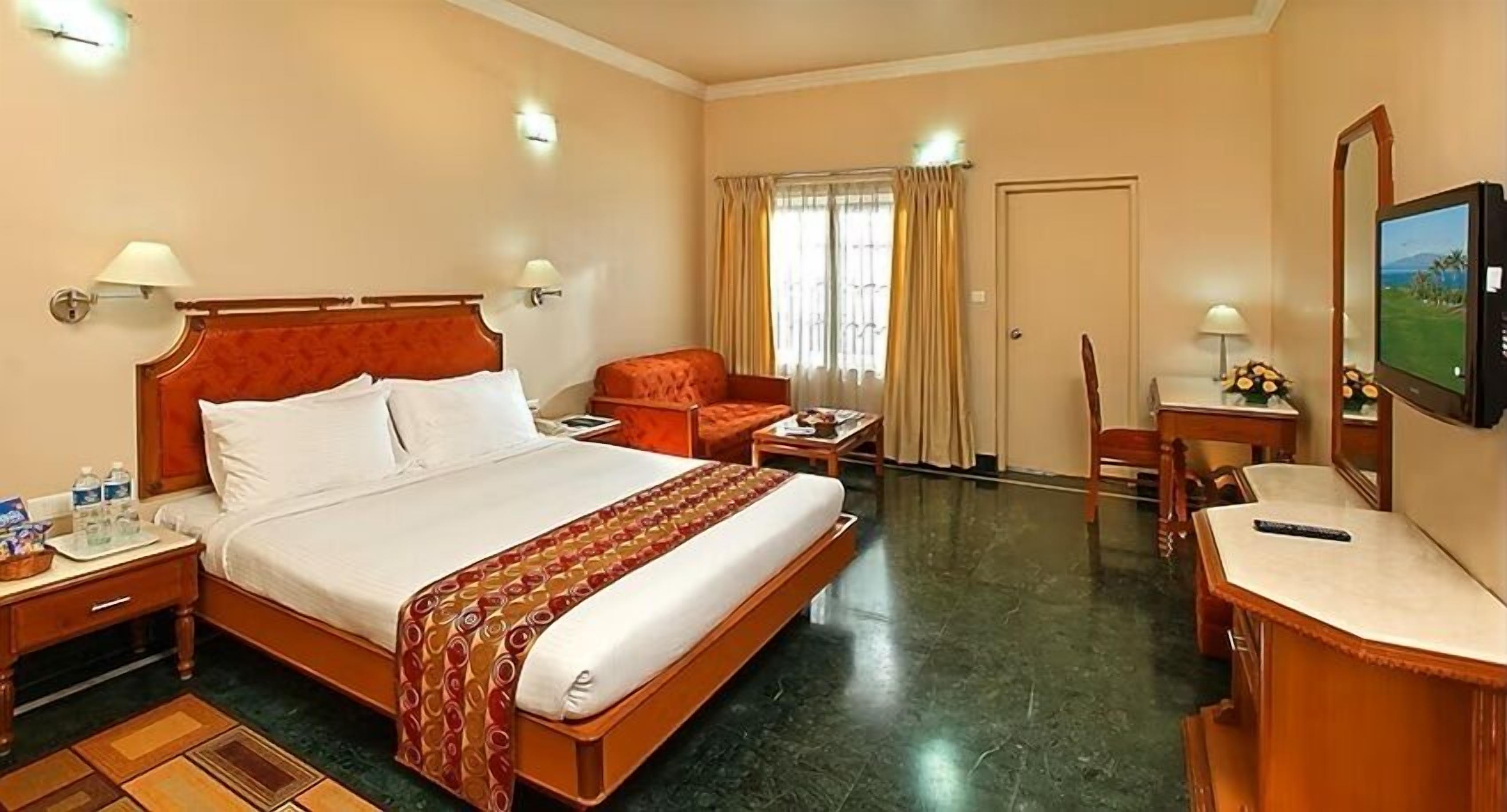 A hotel room with a bed, a desk, a chair, a television, and a window with curtains.