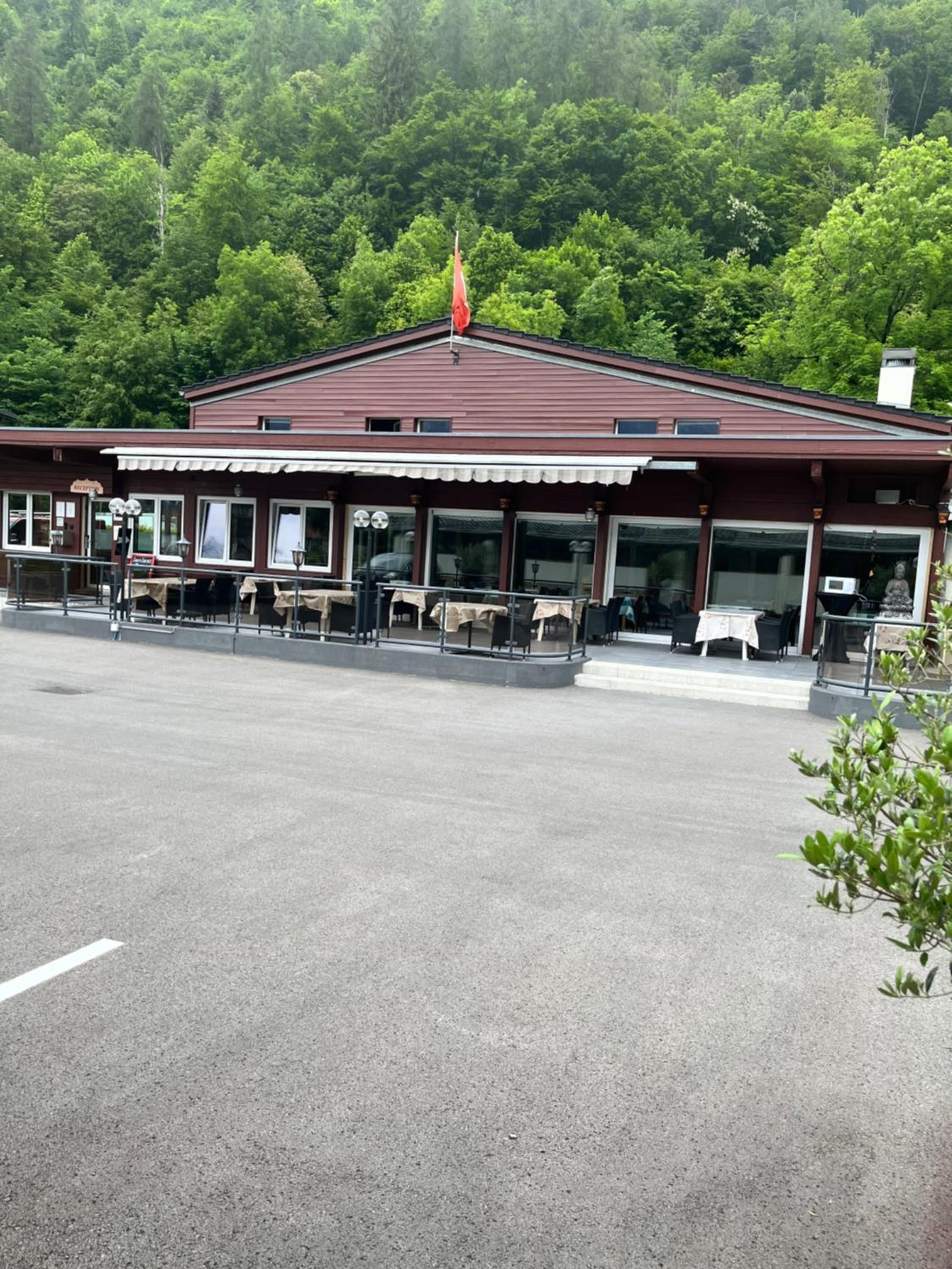 Ein Gebäude mit rotem Dach und einer Fahnenstange, umgeben von einem Parkplatz und Grünflächen.